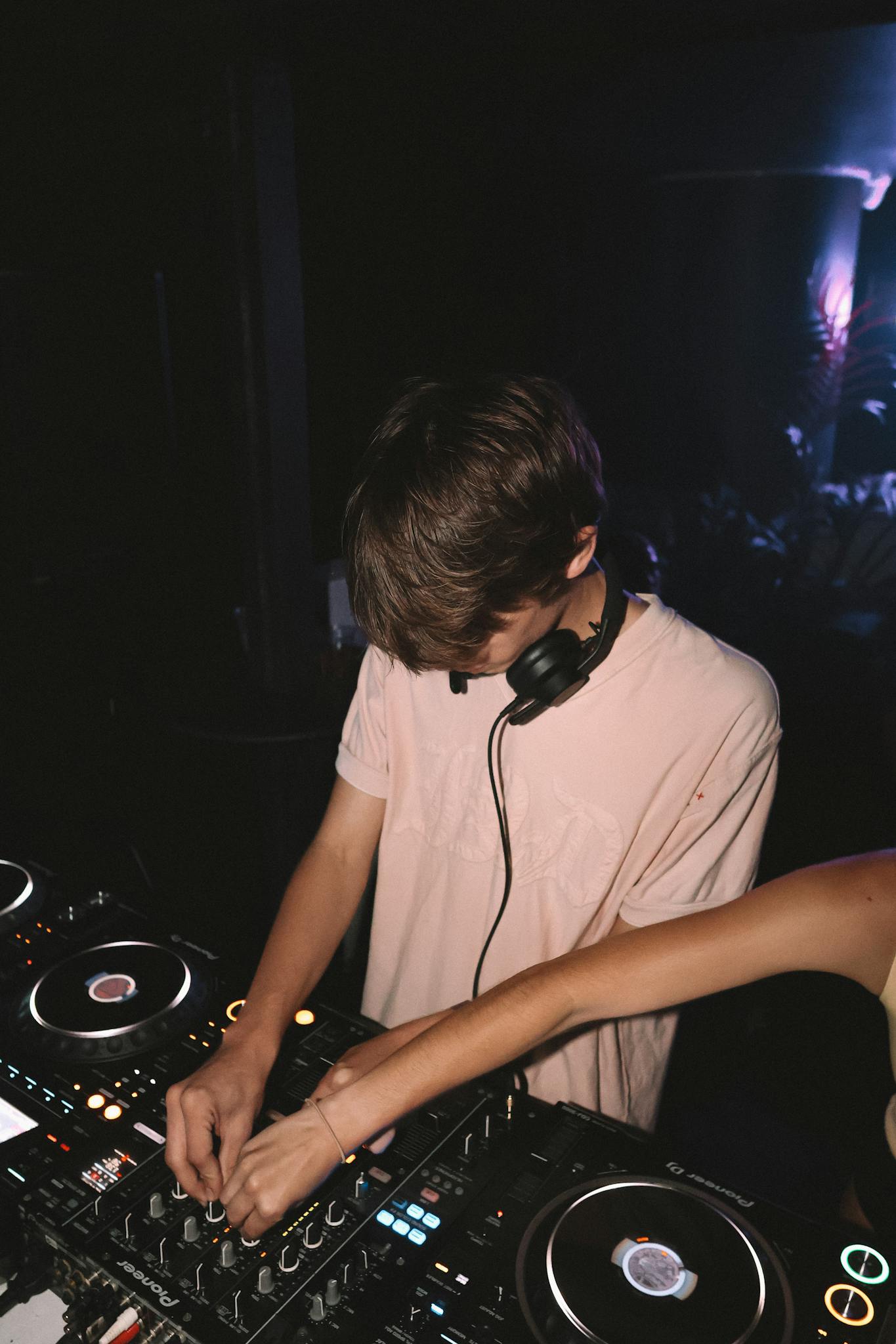 DJ in action at a nightclub, surrounded by vibrant lights and music equipment.